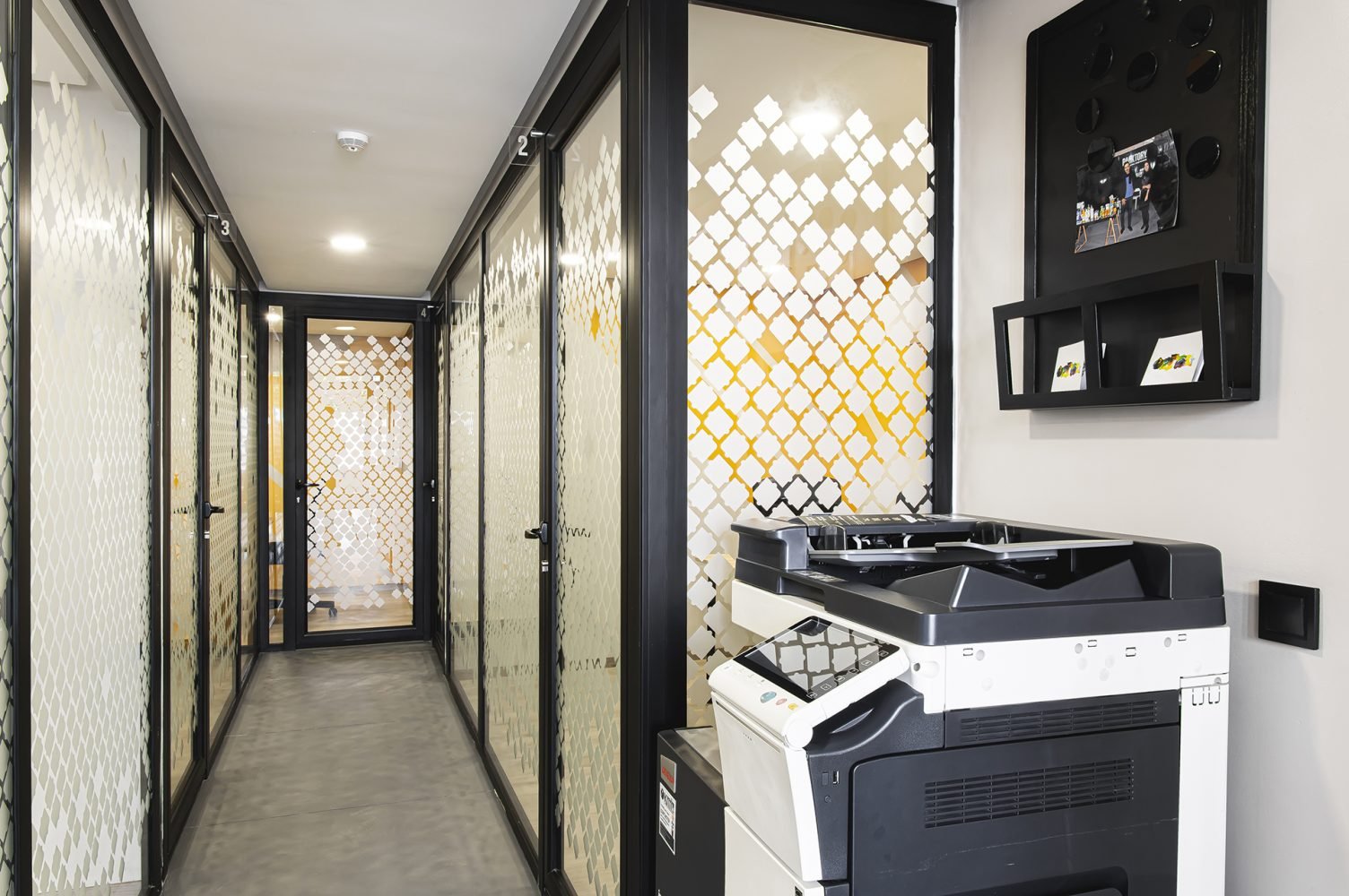 Couloir avec bureaux vitrés et imprimante multifonction chez Mow, espace coworking à Casablanca, offrant des services d'impression et de copie ainsi qu'un environnement de travail pratique et professionnel