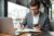 smiling-businessman-eyeglasses-sitting-by-table-cafe-with-laptop-computer-while-using-smartphone-writing-something-scaled