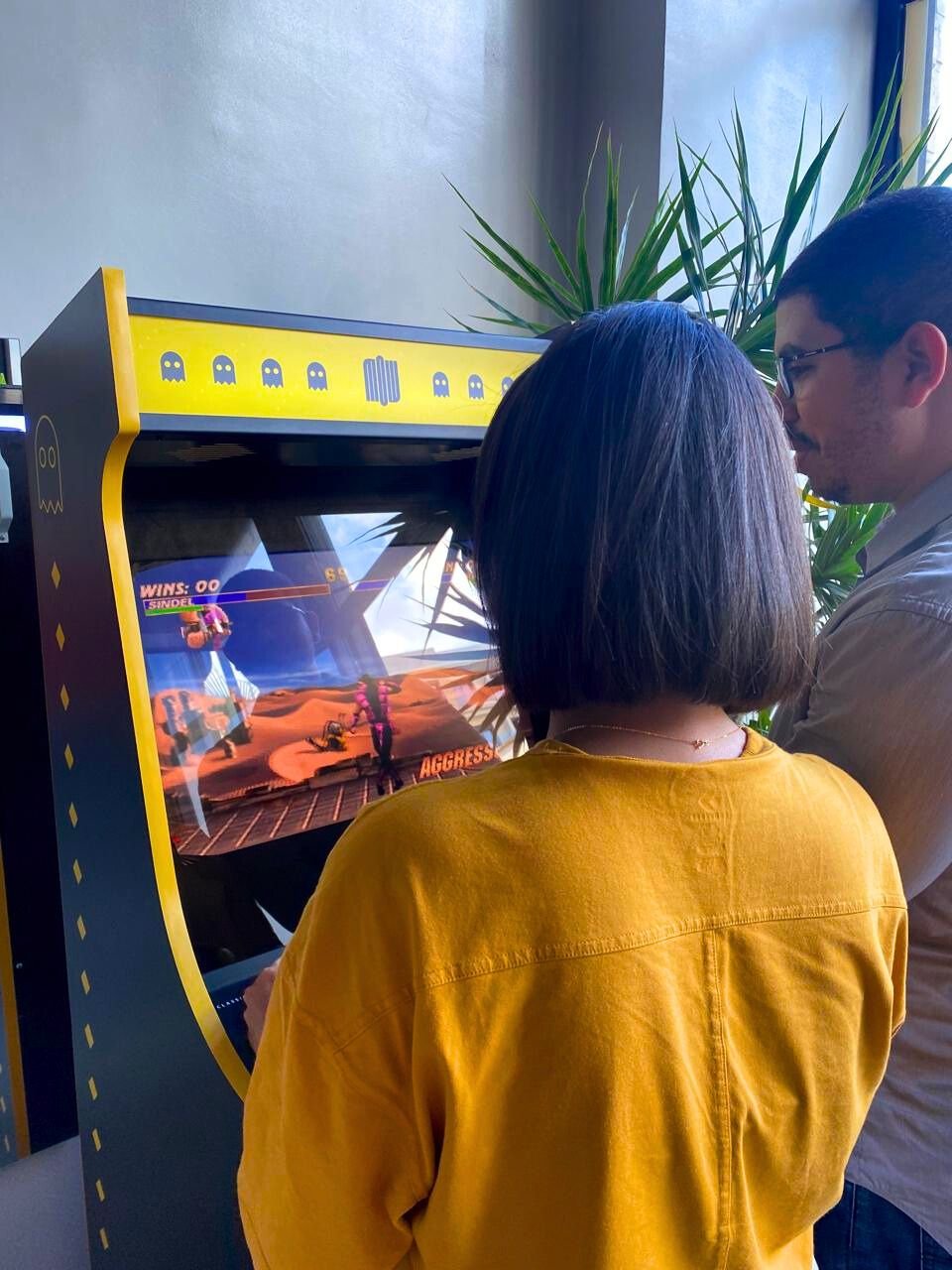 Deux employés de Mow jouant à un jeu vidéo arcade dans un coin détente, favorisant la créativité et le bien-être au travail