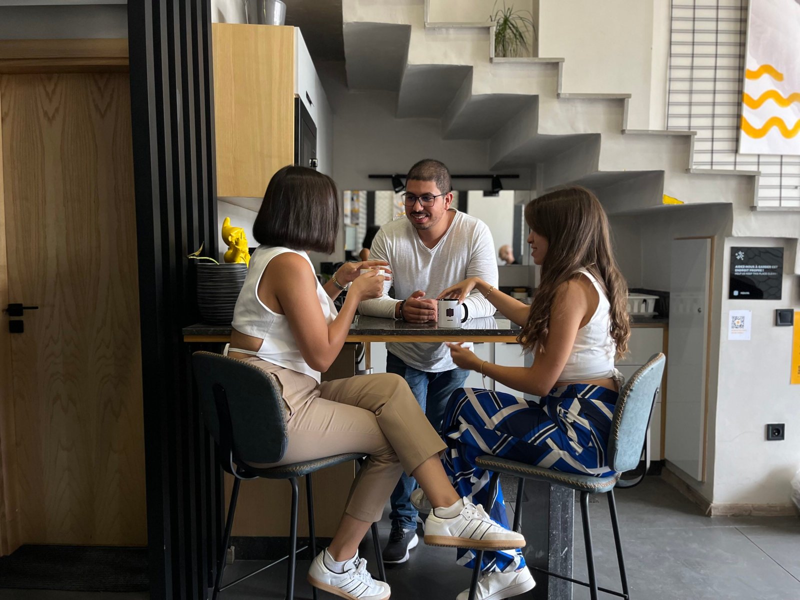 Trois collègues discutent autour d'une table dans l'espace détente moderne de Mow, exprimant des idées lors d'une pause café