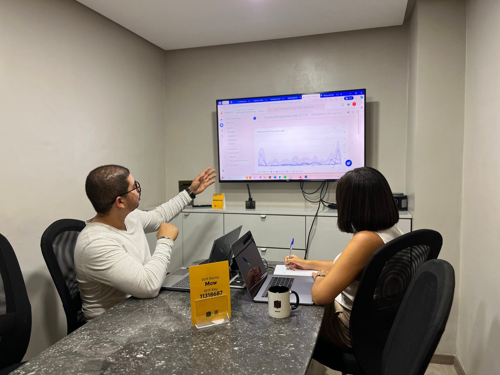 Deux professionnels chez Mow analysant des tendances de données sur un grand écran, discussion stratégique dans une salle de réunion