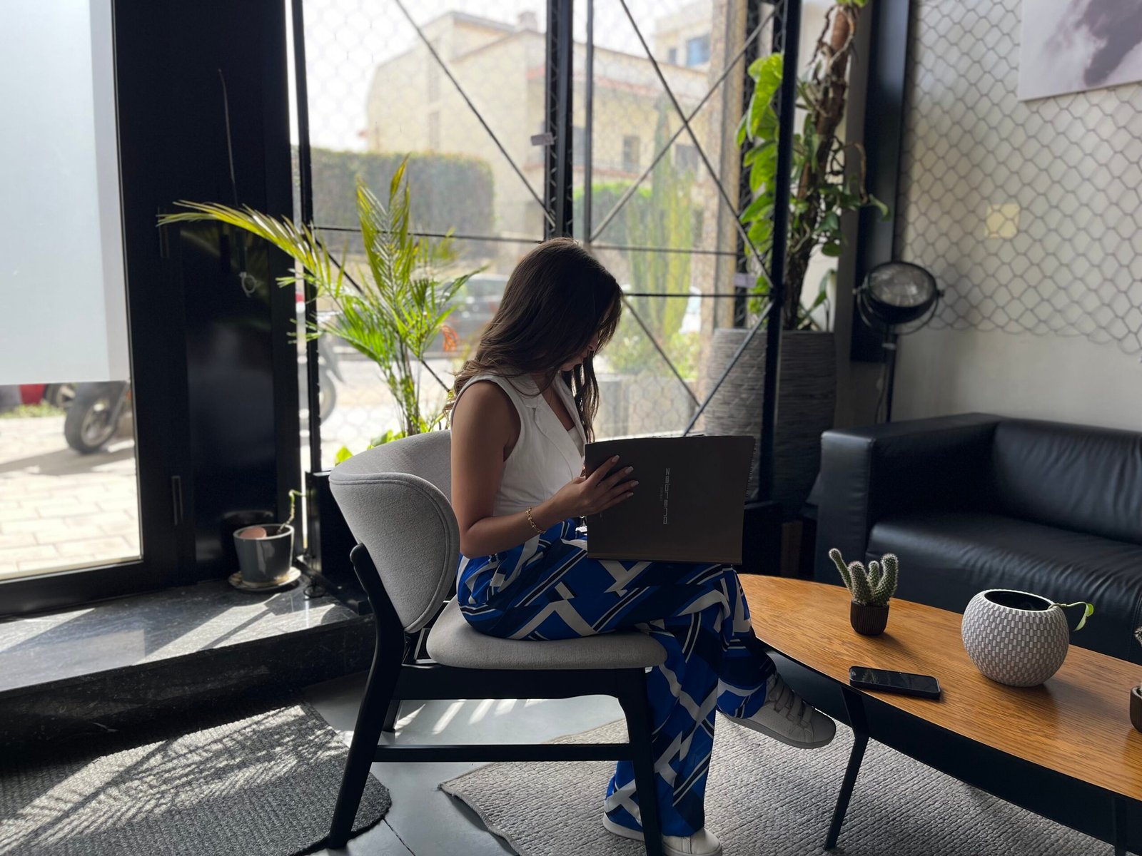 Professionnelle concentrée travaillant sur un ordinateur portable dans un espace lounge moderne et bien éclairé chez Mow, avec une décoration intérieure élégante et des plantes vertes