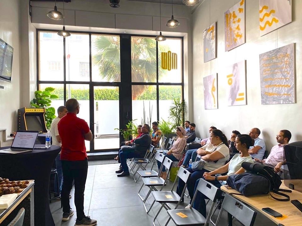 Formateur en rouge donnant un atelier interactif à des employés attentifs dans un espace de bureau lumineux et artistiquement décoré chez Mow