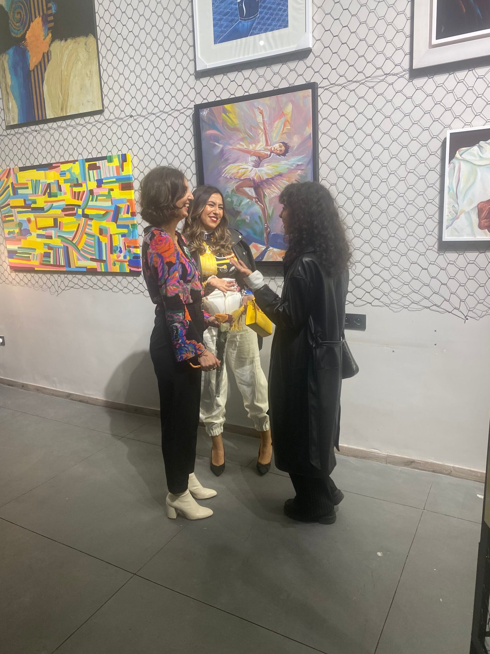 Trois professionnelles en conversation devant une exposition d'art colorée chez Mow, créant un environnement de réseautage dynamique et inspirant