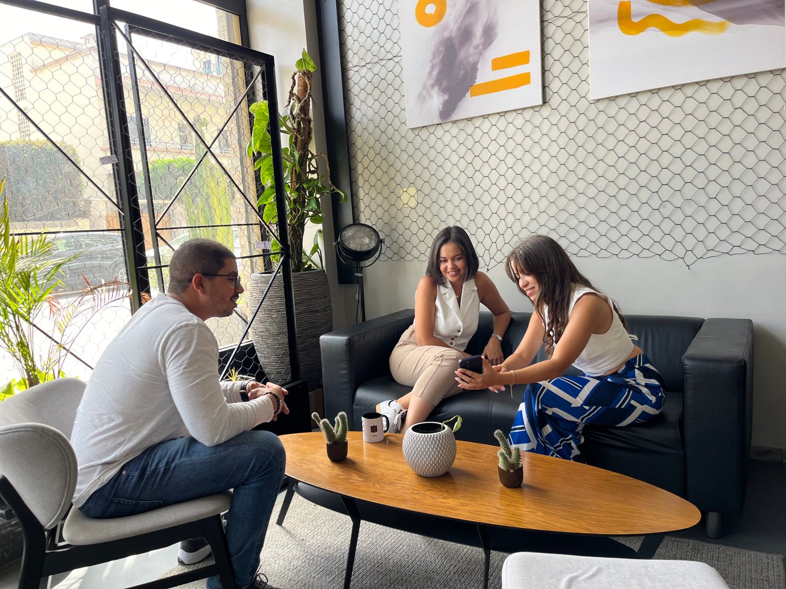 Deux femmes et un homme échangent des idées sur un projet sur un smartphone, assis confortablement dans le salon chic et moderne de Mow