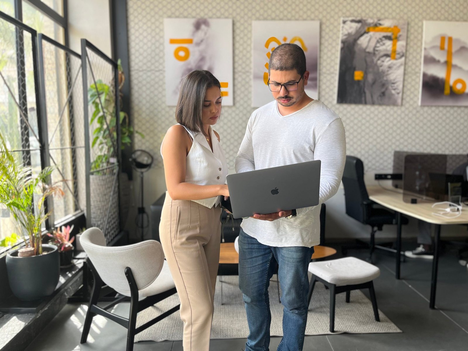 Deux professionnels chez Mow collaborant sur un projet avec un ordinateur portable dans un espace de travail moderne décoré d'art contemporain et de plantes