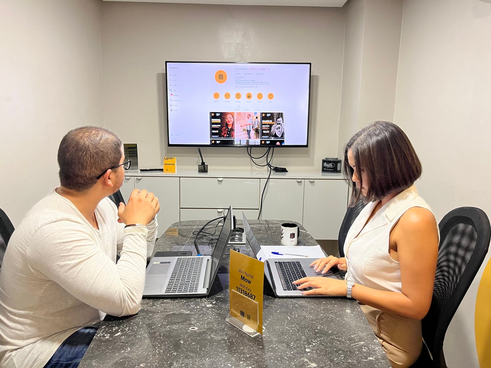 Deux employés de Mow analysant des données sur un grand écran tout en utilisant leurs ordinateurs portables dans une salle de conférence moderne