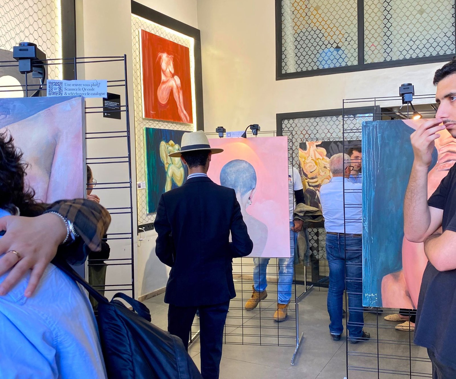 Visiteurs explorant des œuvres d'art lors d'une exposition au coworking MOW à Casablanca, entourés de peintures aux couleurs vibrantes.