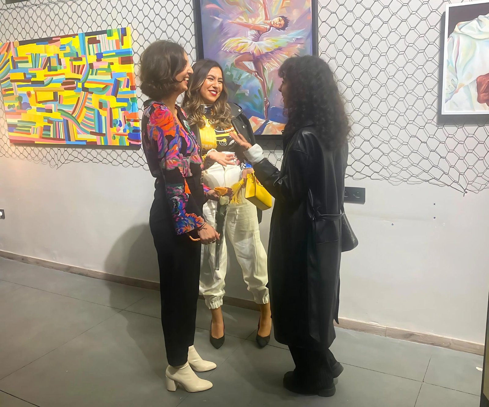 Trois femmes discutant lors d'une exposition artistique au coworking MOW à Casablanca, entourées de peintures colorées.