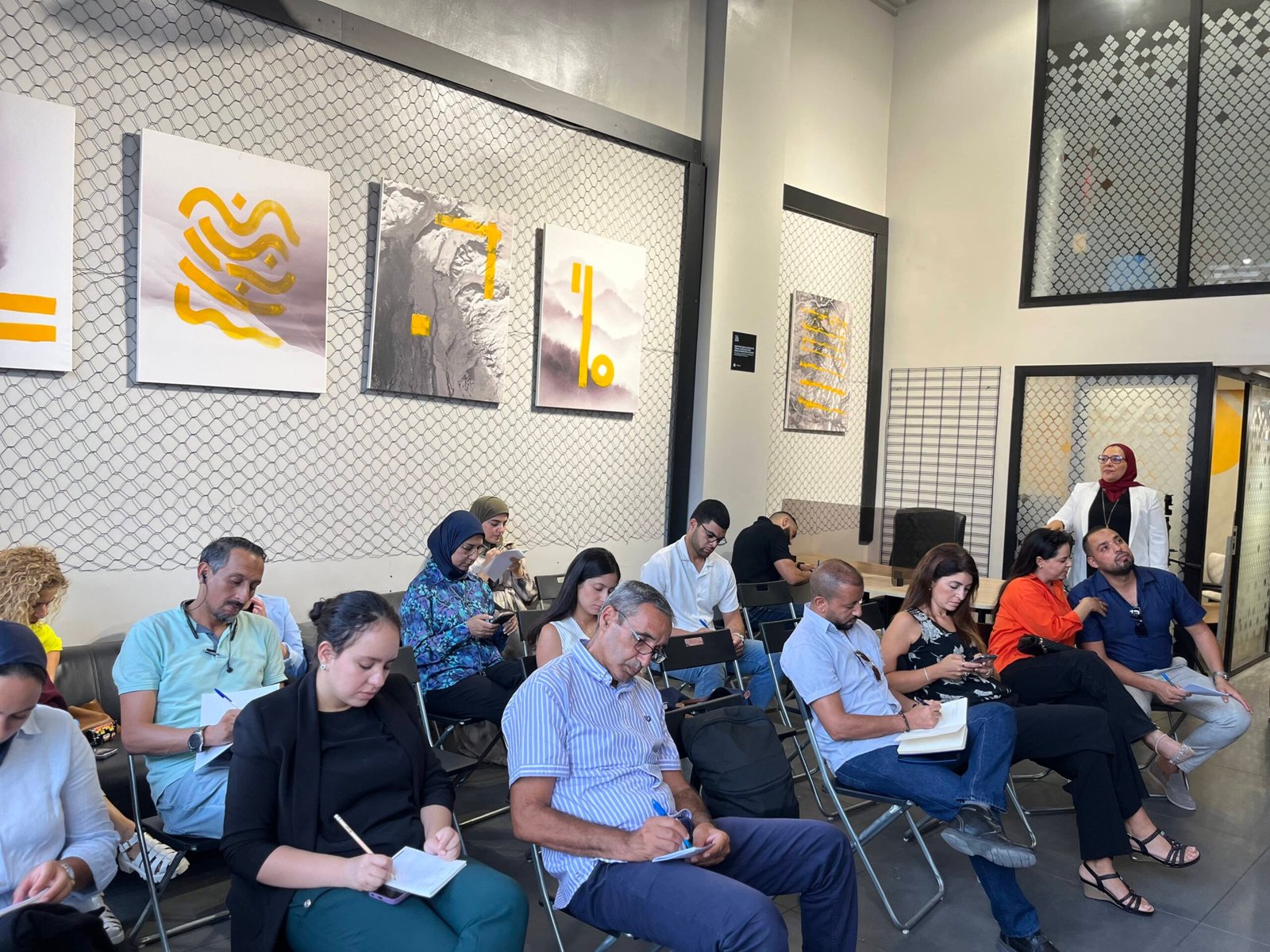 Participants attentifs prenant des notes lors d'un atelier au coworking MOW à Casablanca, avec l'intervenante en arrière-plan.
